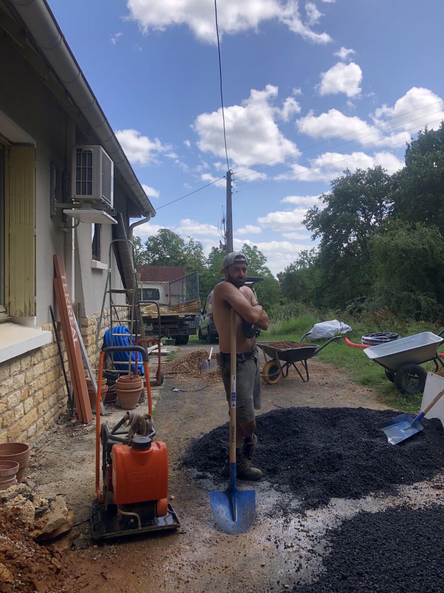 Chantier extérieur près de la maison, avec gravier, pelles et brouettes.