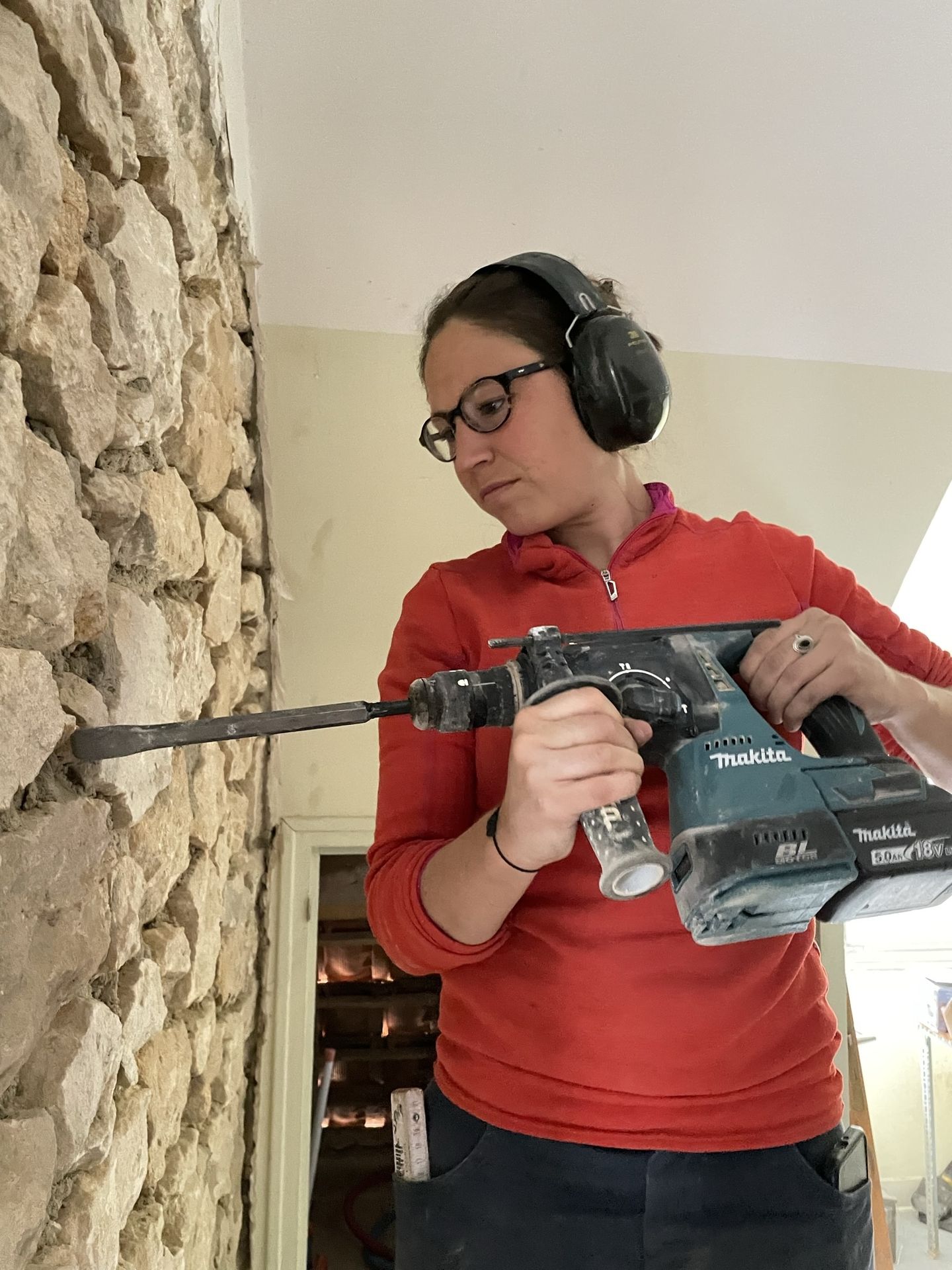 Travail au burineur sur un mur de pierre à l’intérieur de la maison.